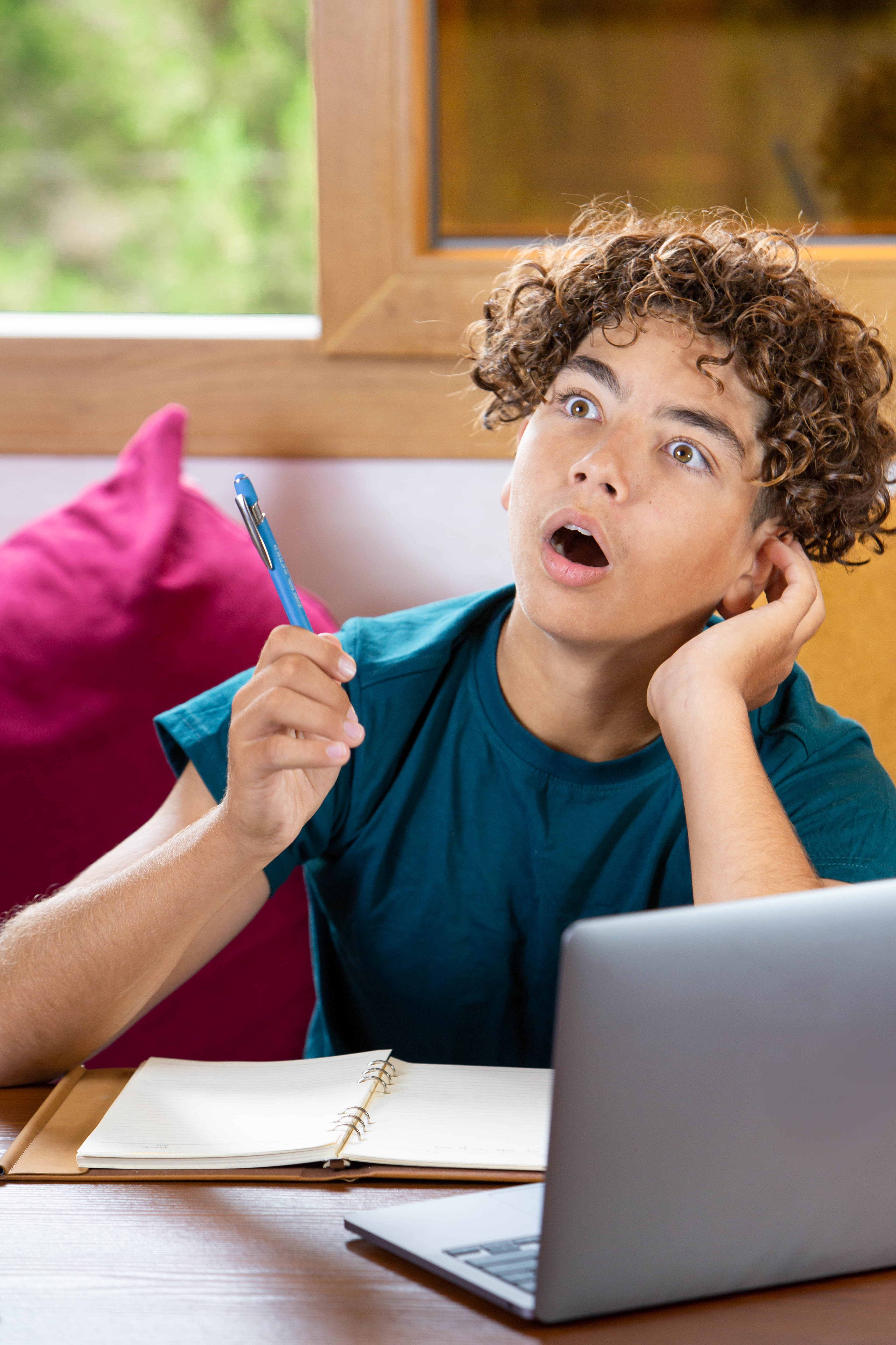 Young student procrastinating while studying at home, looking distracted and overwhelmed by homework, with laptop, notebooks, calculator, apple and hourglass on the desk. Concept of education, stress